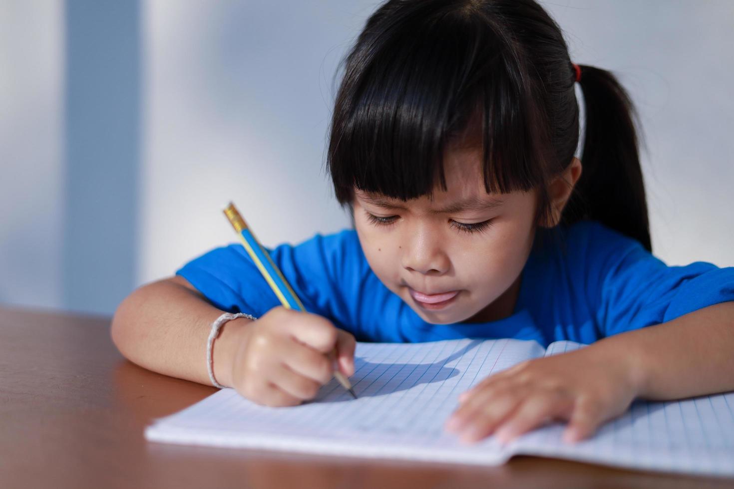 una graziosa bambina asiatica sta scrivendo un libro con una matita sul tavolo. foto