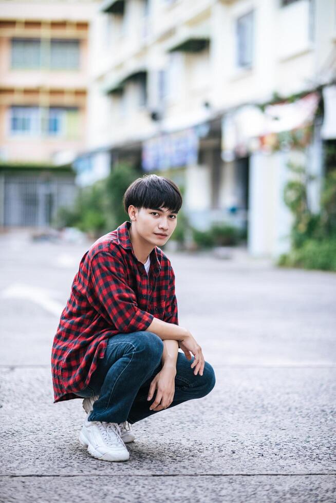 un giovane con una camicia a righe seduto per strada foto