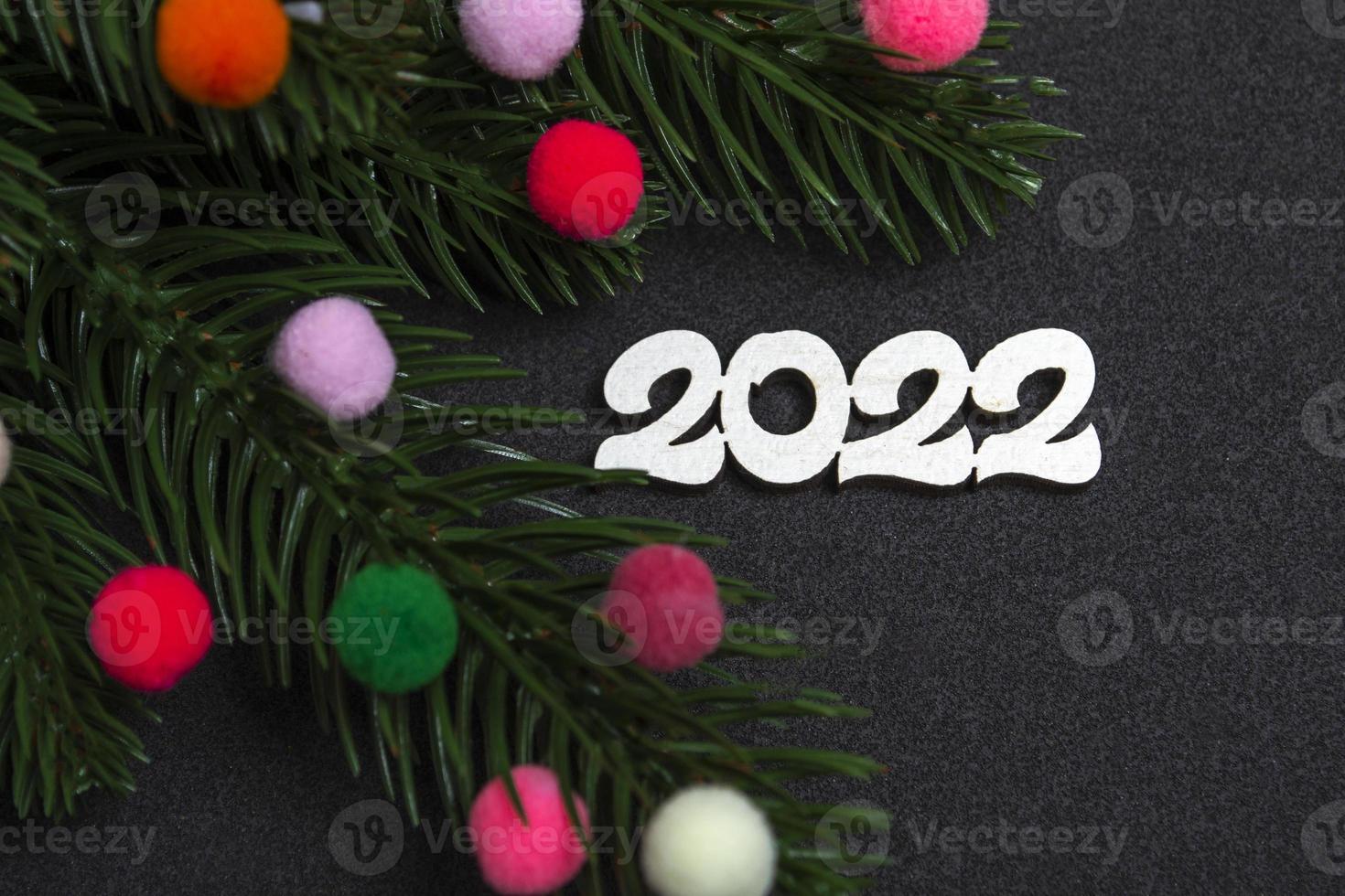 Biglietto natalizio. flatley rami di un albero di natale giocattoli di pelliccia colorati e il numero 2022 su sfondo nero. foto