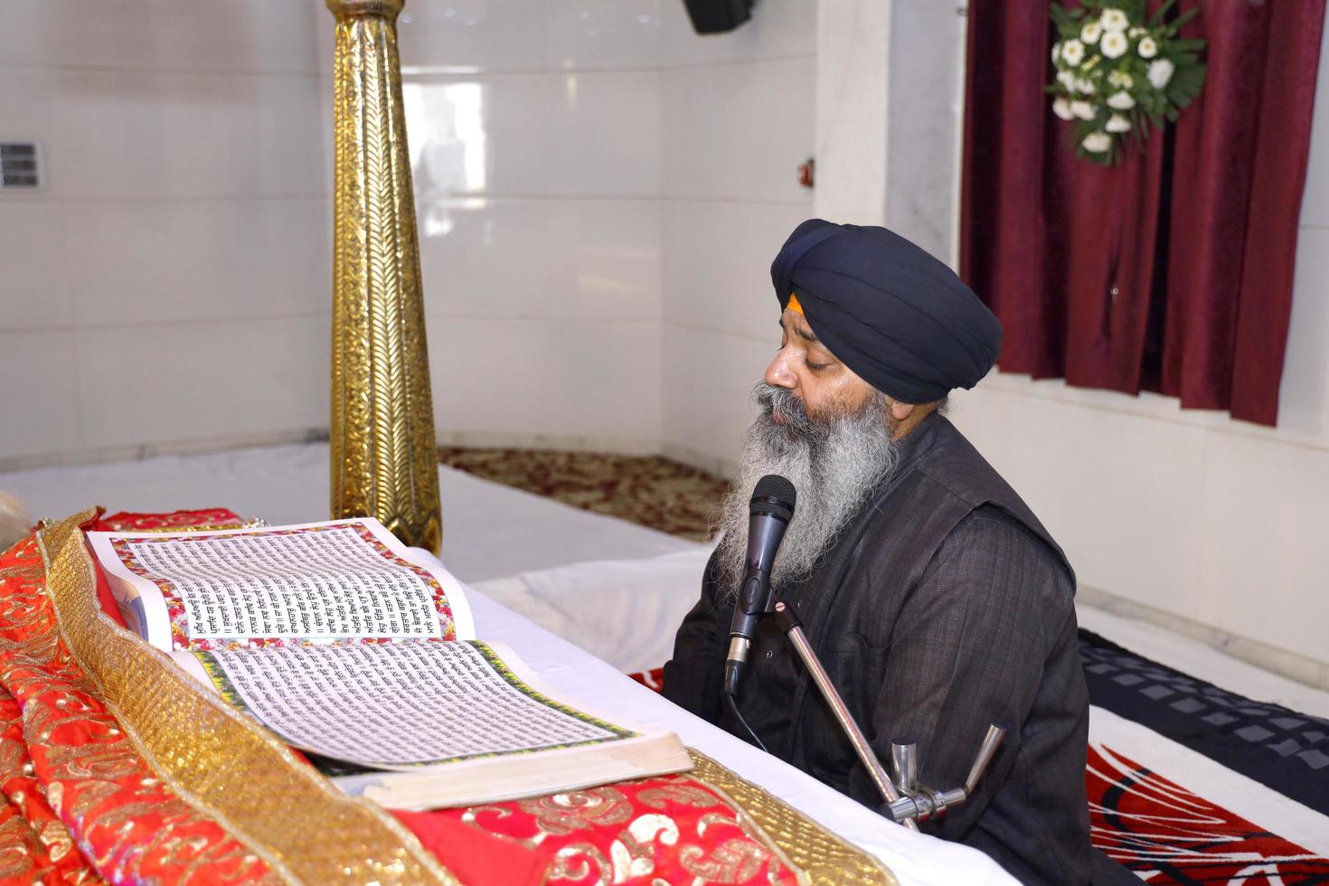 delhi, nuova delhi, india, 2020 - uomo sikh che legge il passaggio dal guru granth sahib seduto all'interno di gurudwara, un luogo di culto per la religione sikh foto