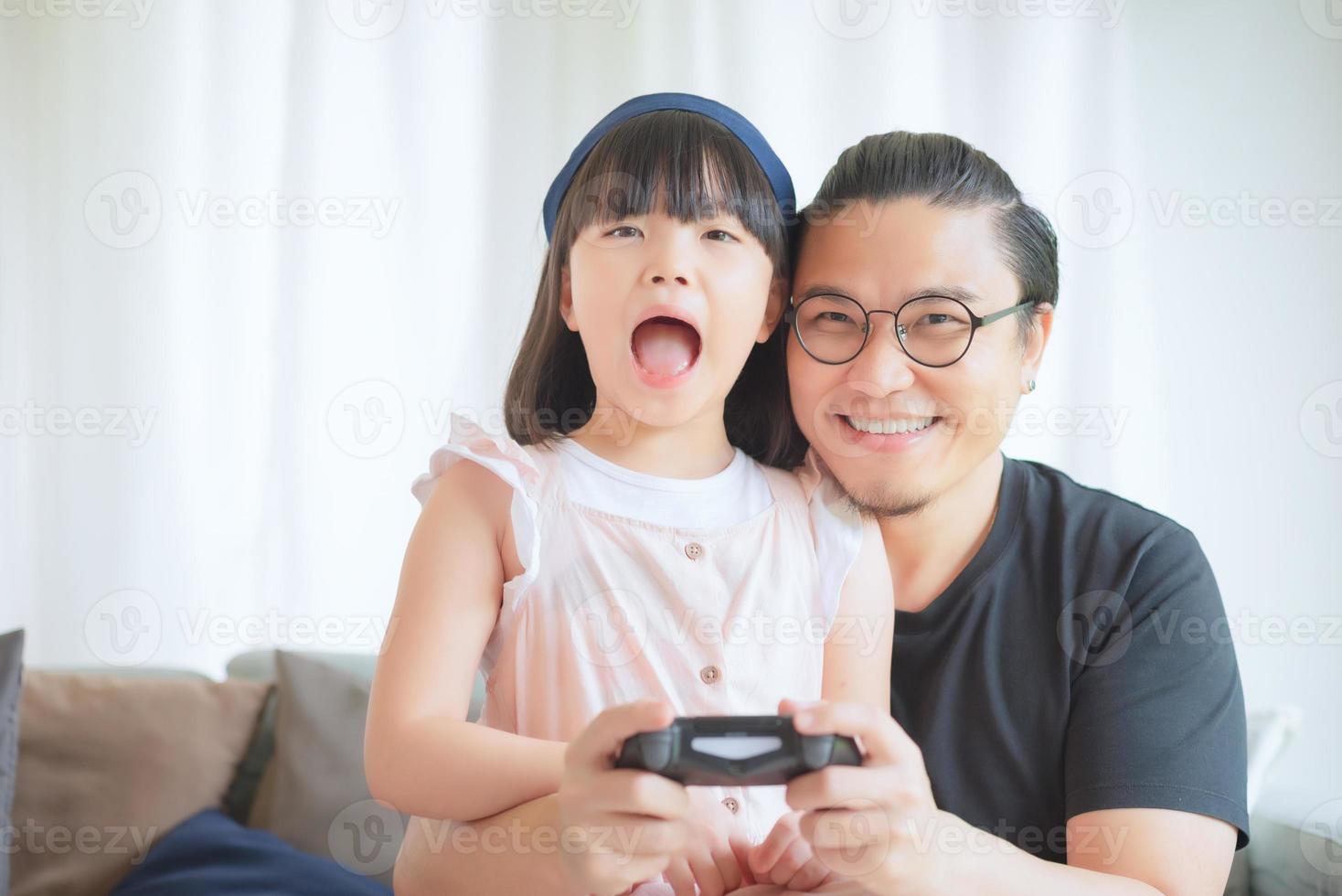 il padre asiatico e la figlia carina si divertono e giocano a giochi per console in vacanza a casa foto