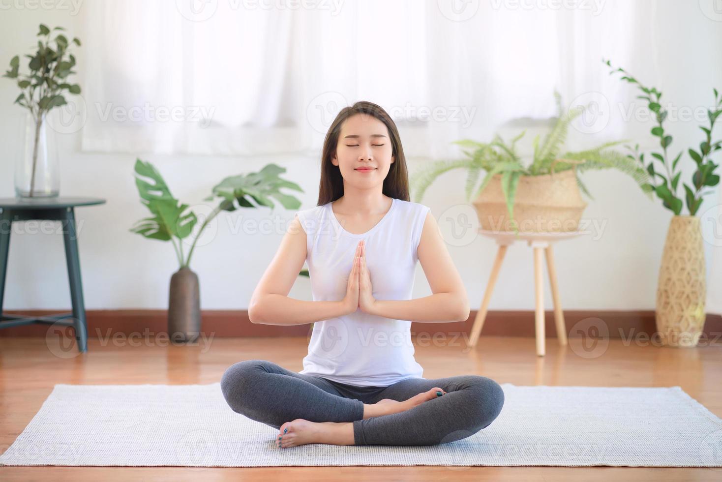 la bella donna asiatica mantiene la calma e medita mentre pratica lo yoga a casa per uno stile di vita sano di tendenza foto