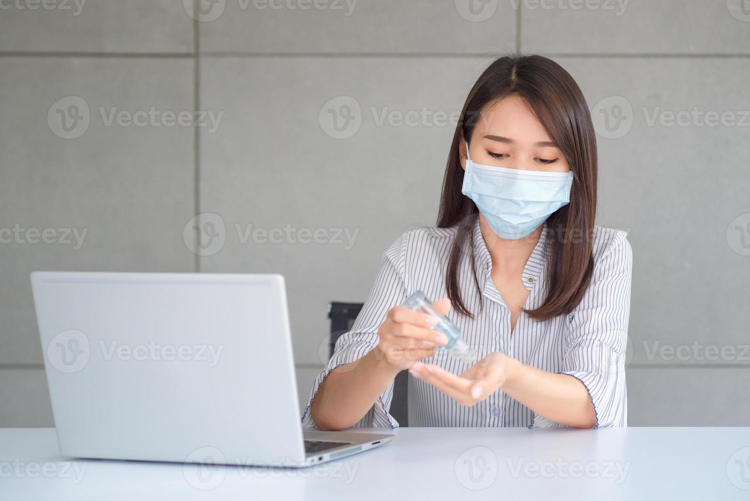 donna d'affari che indossa una maschera e usa un disinfettante personale per pulirsi la mano in ufficio per mantenere l'igiene.preventivo durante il periodo di epidemia da coronavirus o covid19. foto
