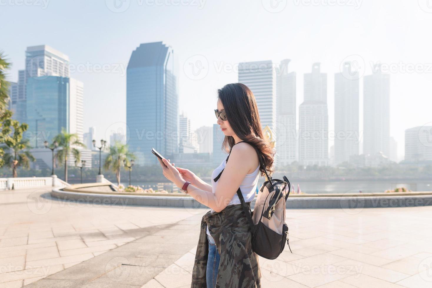 bella donna turistica asiatica che guarda il telefono cellulare per cercare la posizione del punto di riferimento. viaggio di vacanza in estate foto