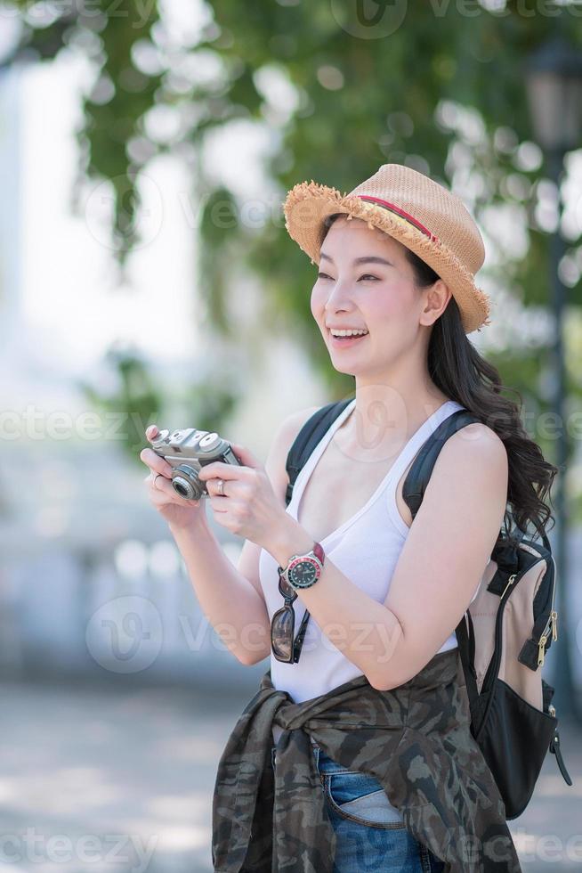 la bella donna turistica asiatica si diverte a scattare foto con la fotocamera retrò in un punto turistico. viaggio di vacanza in estate.