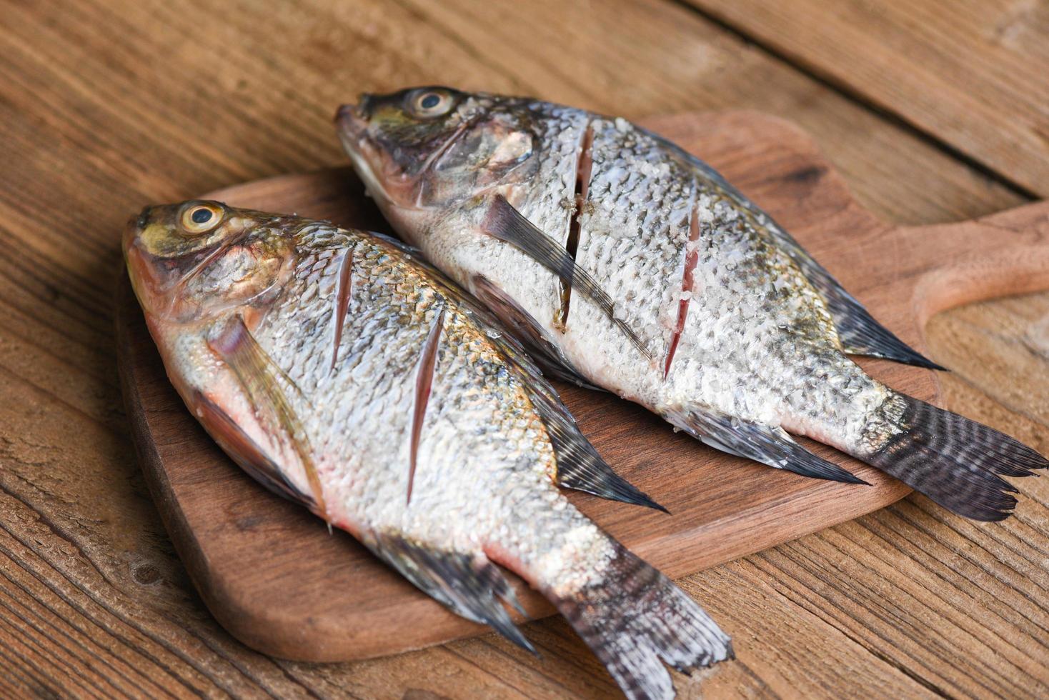 pesce fresco di tilapia per cucinare il cibo - due pesci d'acqua dolce crudi di tilapia del nilo su tavola di legno foto