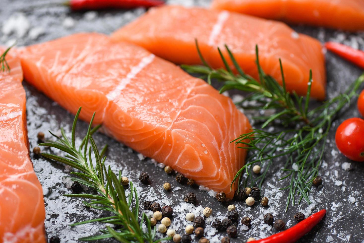 filetto di salmone crudo con erbe e spezie su sfondo nero scuro foto