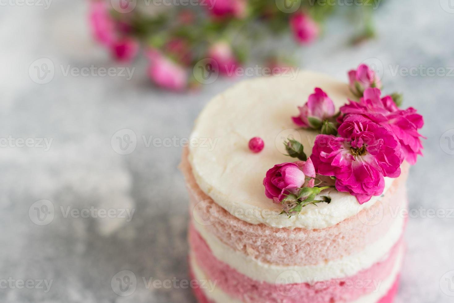 una piccola torta bianca e rosa decorata con fiori e frutti di bosco foto