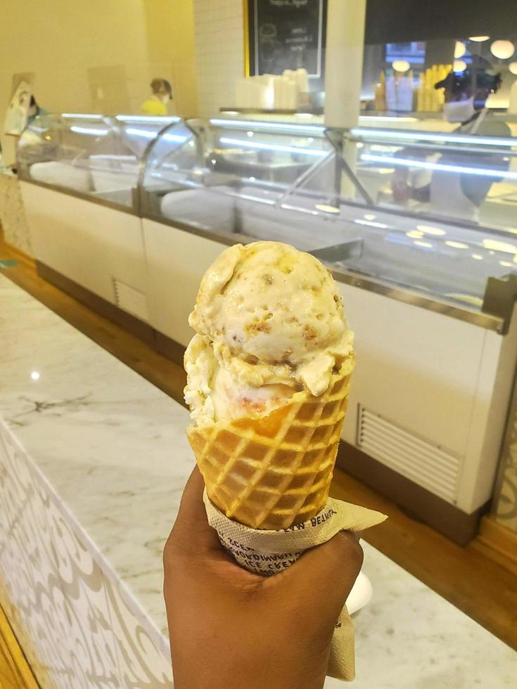 gelato al gusto di cioccolato bianco dessert congelato modello in cono di cialda che tiene la mano sul tavolo. foto