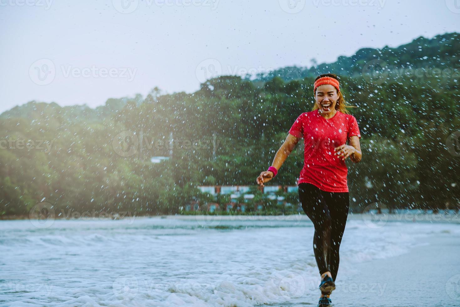 donna asiatica jogging allenamento sulla spiaggia al mattino. rilassati con la spiaggia. divertente e felice di giocare, saltare, prendere a calci il mare. in estate foto