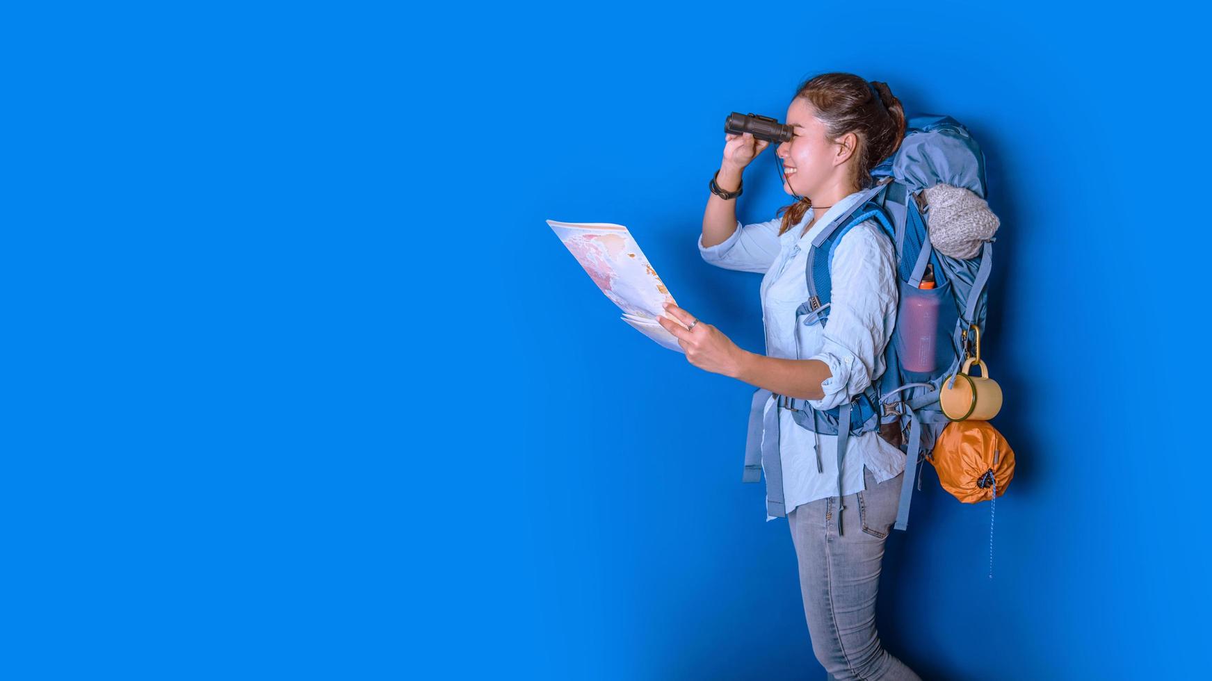 giovane viaggiatore asiatico donna felice in camicia blu con zaino con e attrezzatura per le vacanze dei viaggiatori con una mappa, su sfondo di colore blu. zaino da viaggio foto