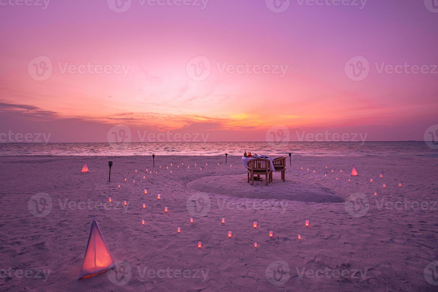 bellissimo tavolo allestito per una cena romantica sulla spiaggia con lanterne e sedie e fiori con candele e cielo e mare sullo sfondo. cena in spiaggia al tramonto foto