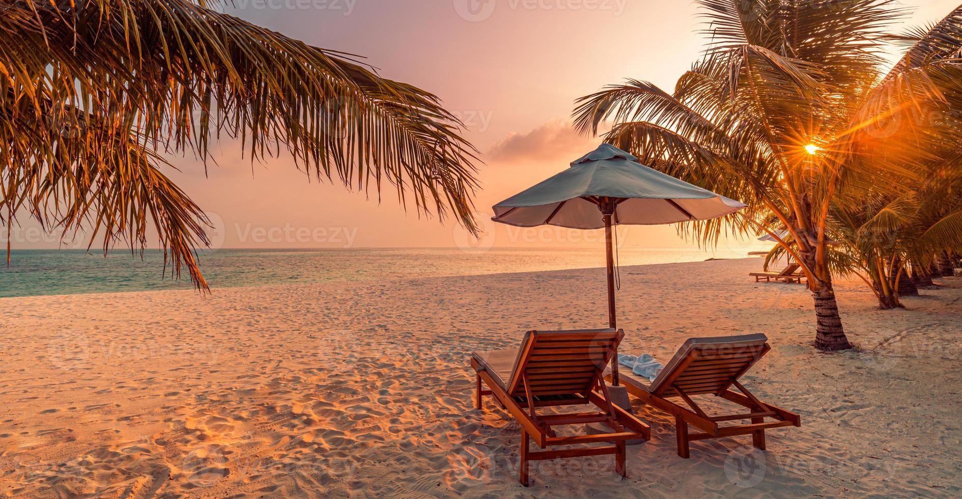 bellissimo scenario del tramonto tropicale, due lettini, lettini, ombrellone sotto la palma. sabbia bianca, vista mare con orizzonte, cielo crepuscolare colorato, calma e relax. hotel ispiratore del resort sulla spiaggia foto