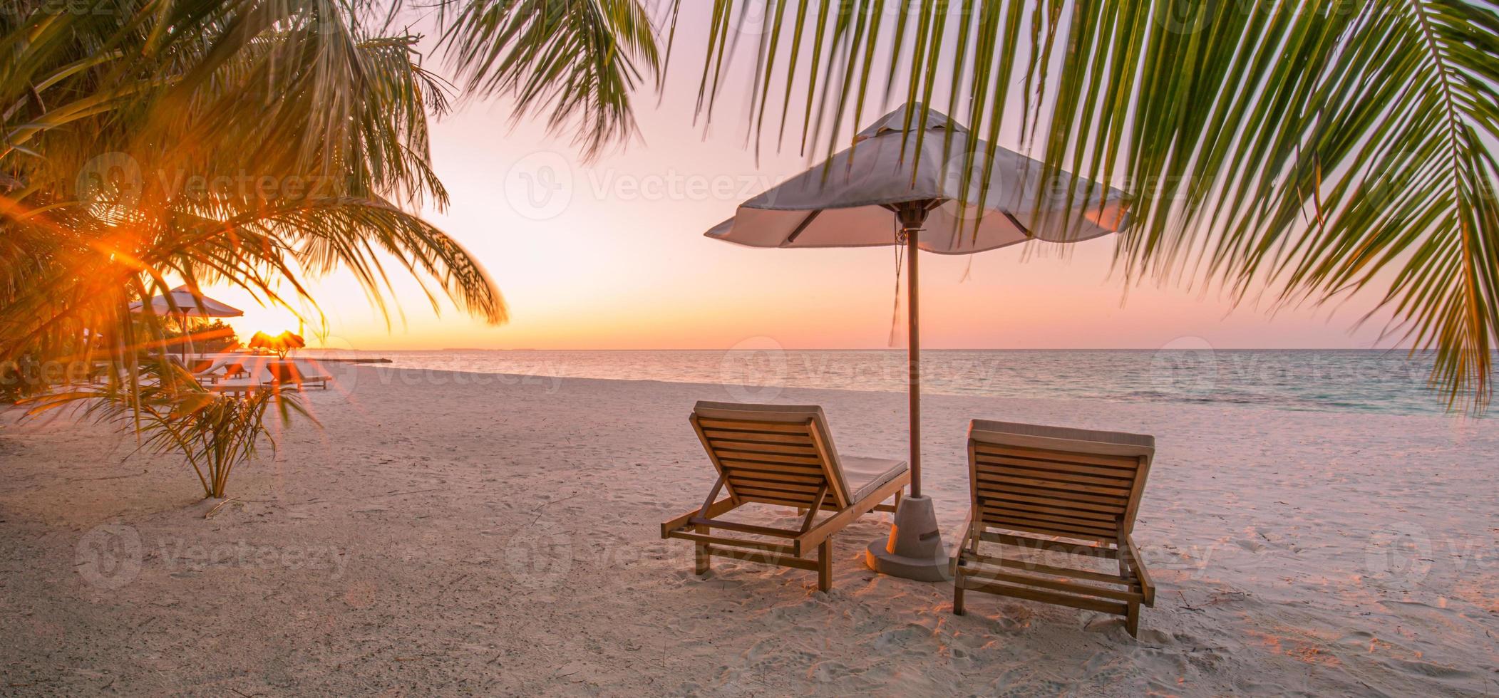 bellissimo scenario del tramonto tropicale, due lettini, lettini, ombrellone sotto la palma. sabbia bianca, vista mare con orizzonte, cielo crepuscolare colorato, calma e relax. hotel ispiratore del resort sulla spiaggia foto