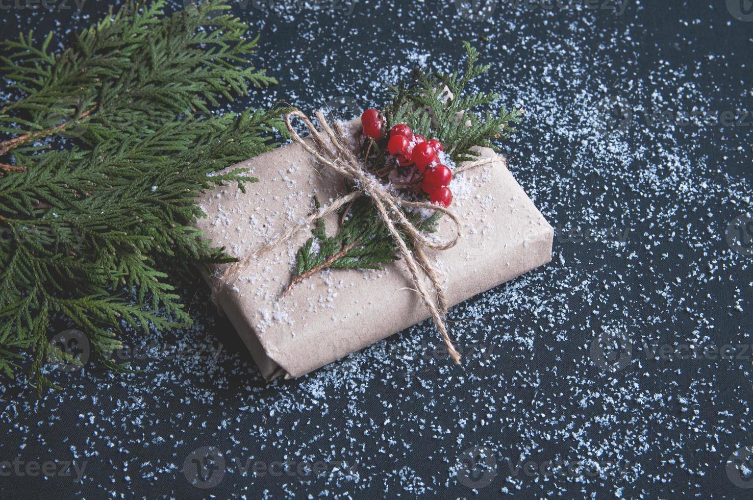 confezione regalo di natale in carta kraft con neve su un tavolo nero con rami di abete. foto