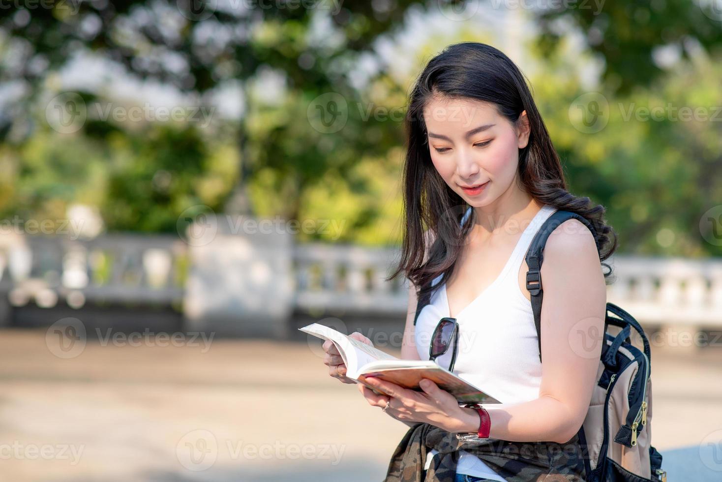 bella donna turistica asiatica che legge la guida di viaggio alla ricerca di luoghi turistici per i turisti. viaggio di vacanza in estate. foto