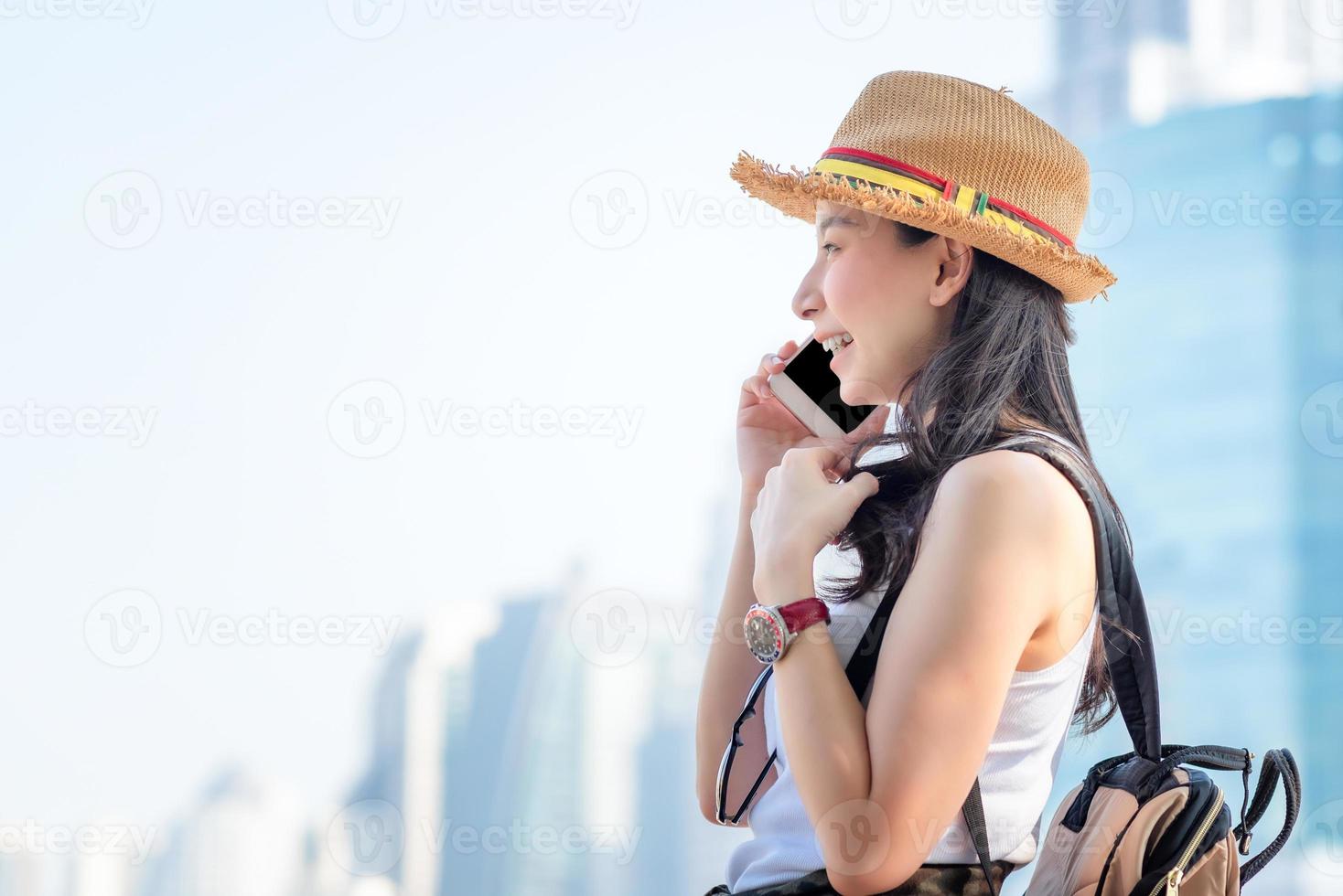 bella donna asiatica turistica solista che sorride e si diverte a parlare tramite telefono cellulare nel centro della città. viaggio di vacanza in estate. foto