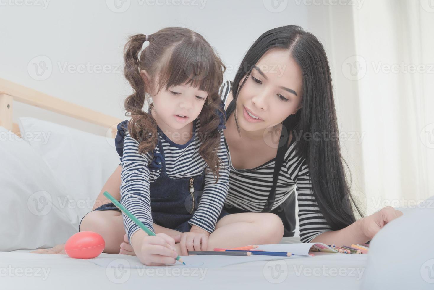 famiglia felice in camera da letto, madre asiatica che insegna a sua figlia a imparare per la scuola materna. design fotografico per il concetto di famiglia, bambini e persone felici. foto