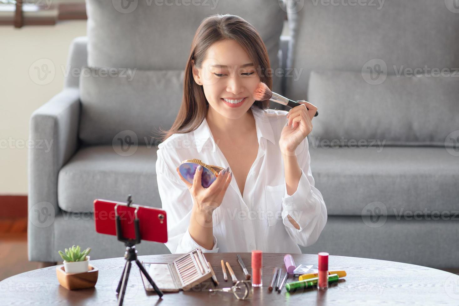 influencer di bellezza femminile asiatica che realizza un video tutorial per il suo canale di bellezza sui cosmetici durante il soggiorno al sicuro a casa foto