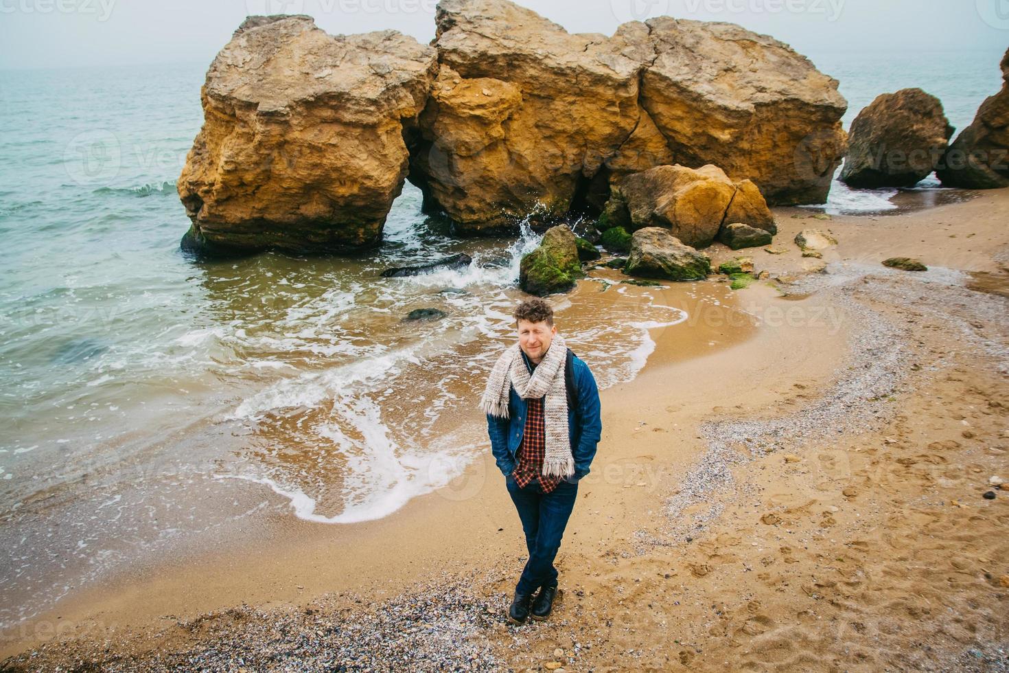 uomo viaggiatore con zaino in piedi sulla spiaggia sabbiosa in mezzo alle rocce sullo sfondo del mare foto