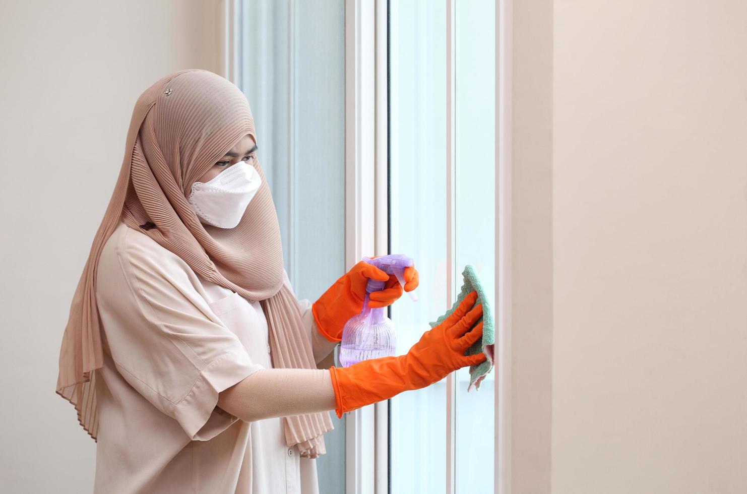 donna musulmana che pulisce il vetro della porta con tessuto e spray alcolico. foto