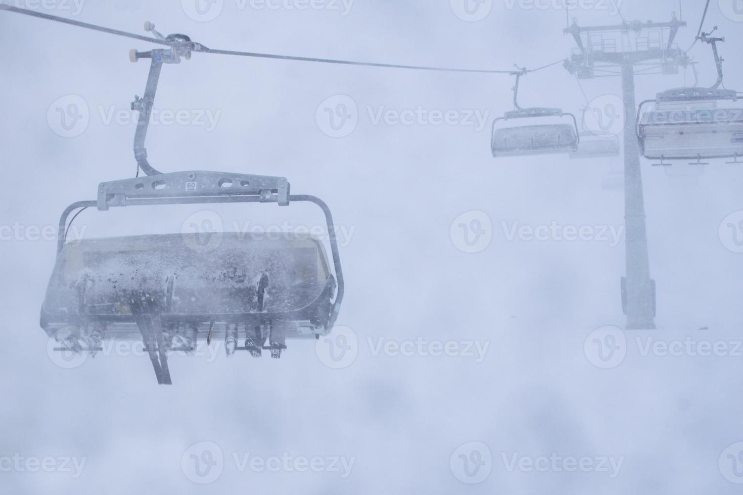 tre persone con gli sci siedono sulla seggiovia della stazione sciistica in condizioni invernali tempestose. Cattiva visibilità e tempo nel concetto di stazione sciistica. foto
