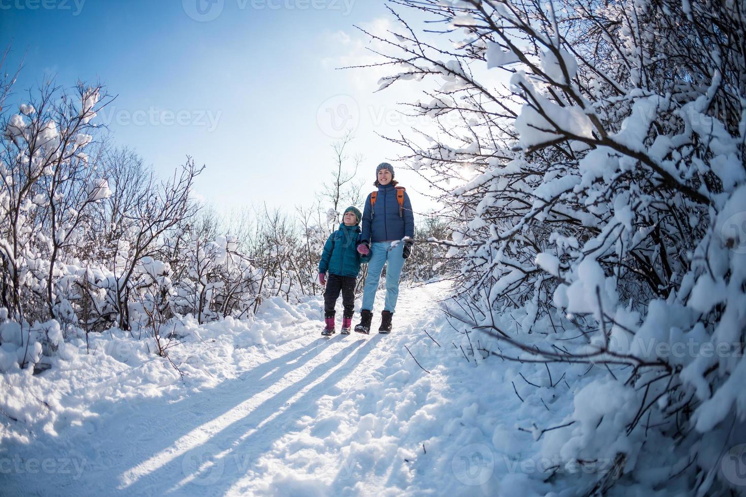 un bambino con uno zaino cammina con la madre in un bosco innevato foto