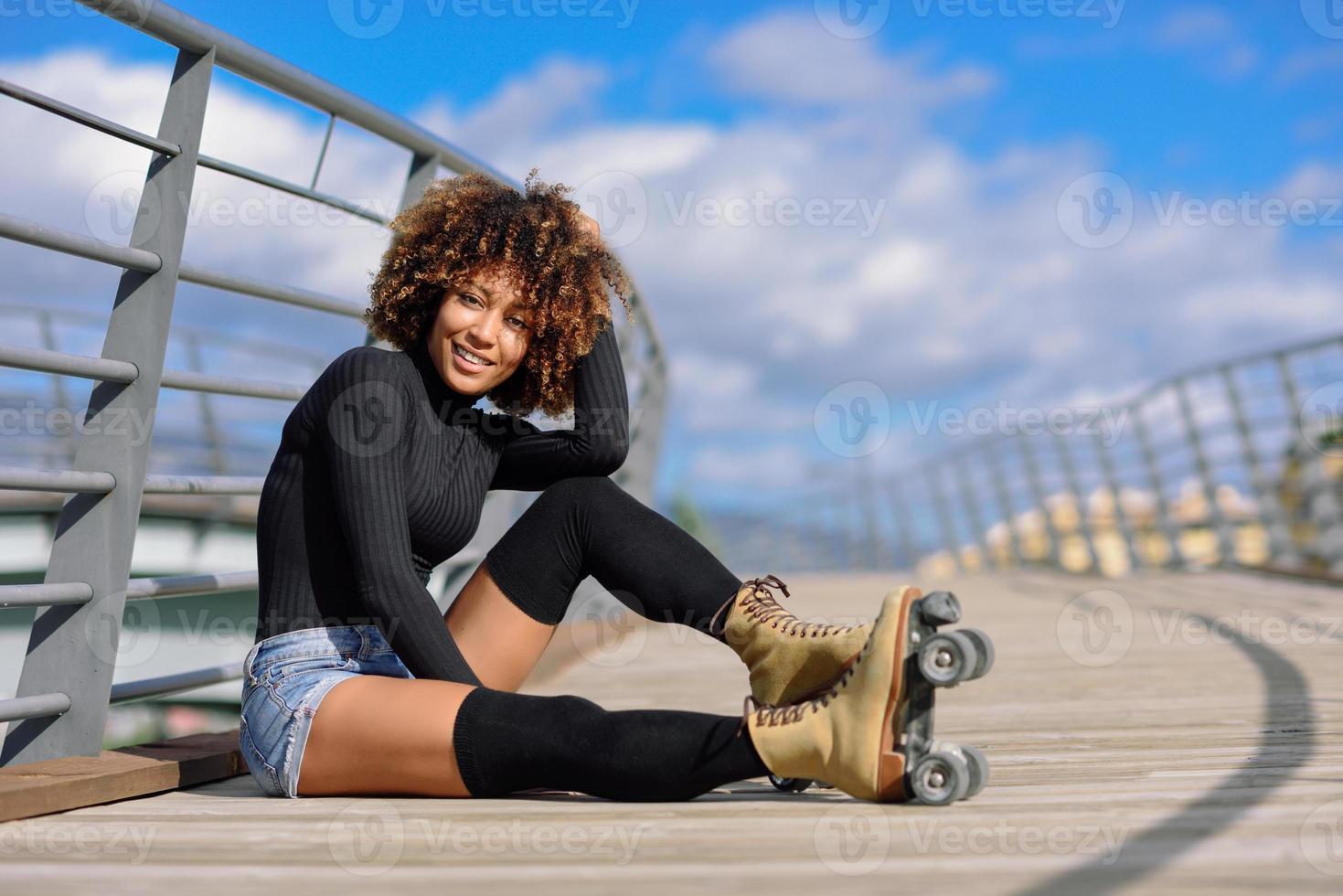 acconciatura afro donna su pattini a rotelle seduta su un ponte urbano foto