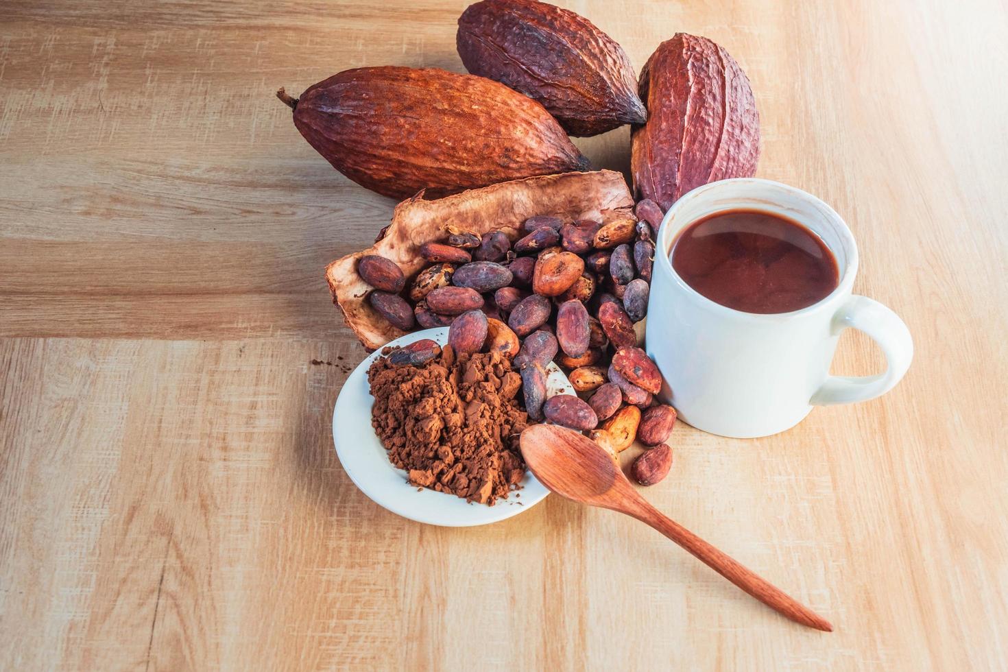 tazza di cioccolata calda con cacao in polvere e fave di cacao su fondo in legno foto