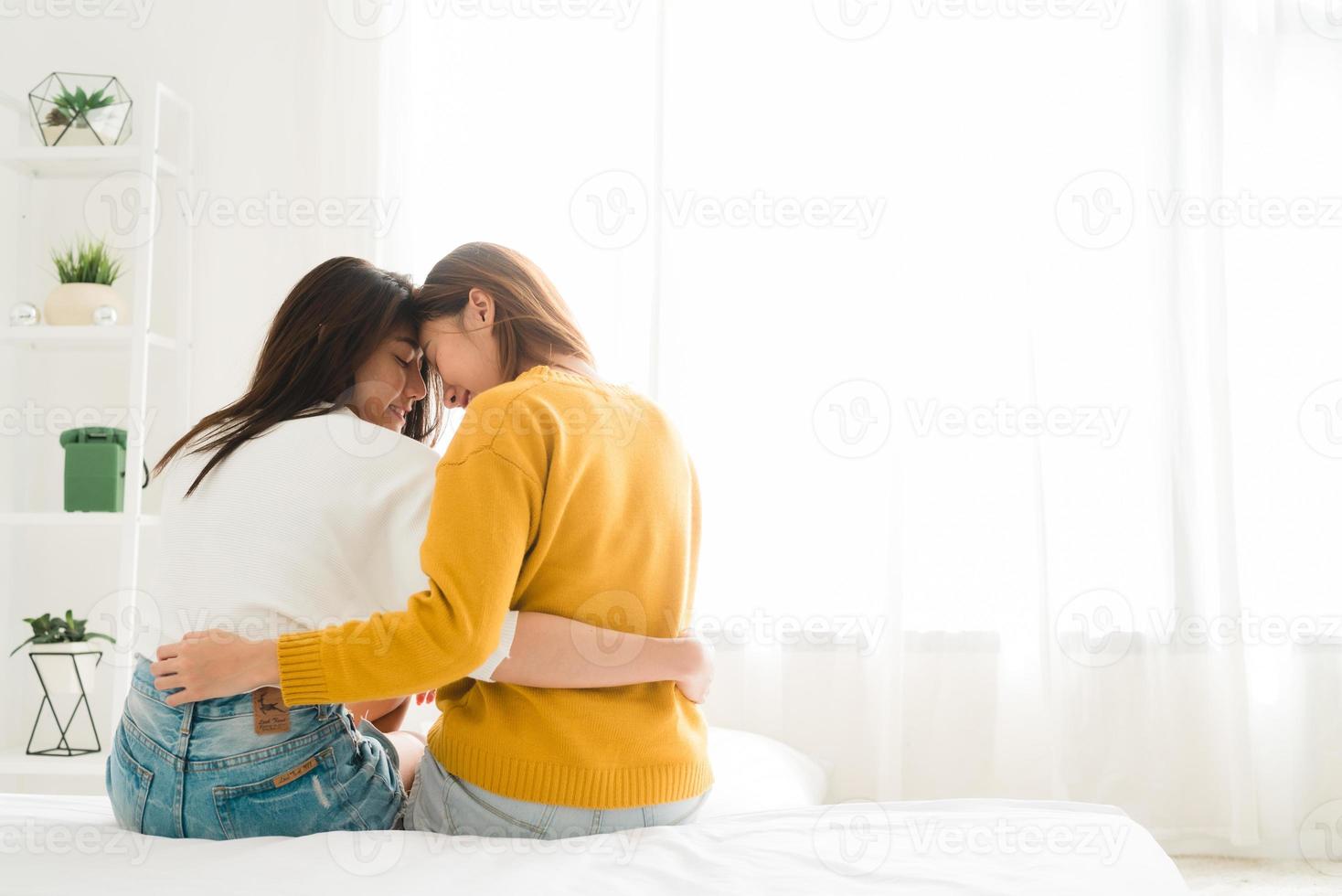 vista posteriore delle donne coppia lesbica felice che si sveglia al mattino, seduta sul letto, che si estende nell'accogliente camera da letto, guardando attraverso la finestra. donne divertenti dopo il risveglio. lgbt coppia lesbica insieme al chiuso concept foto