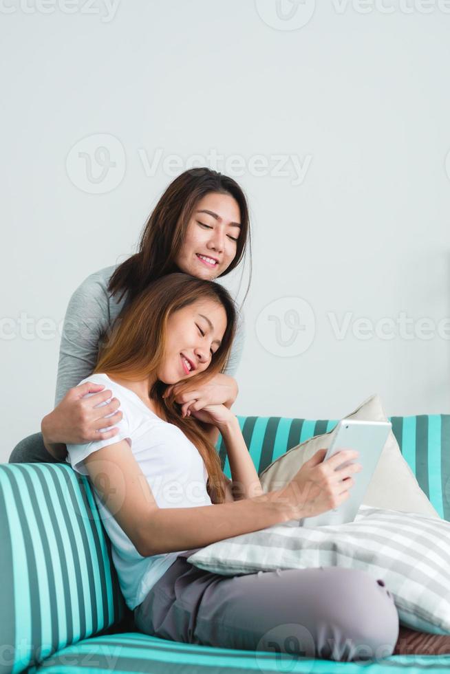 belle giovani donne asiatiche lgbt lesbica coppia felice seduta sul divano acquisto online utilizzando tablet nel soggiorno di casa. lgbt coppia lesbica insieme al chiuso concetto. passare del tempo piacevole a casa. foto