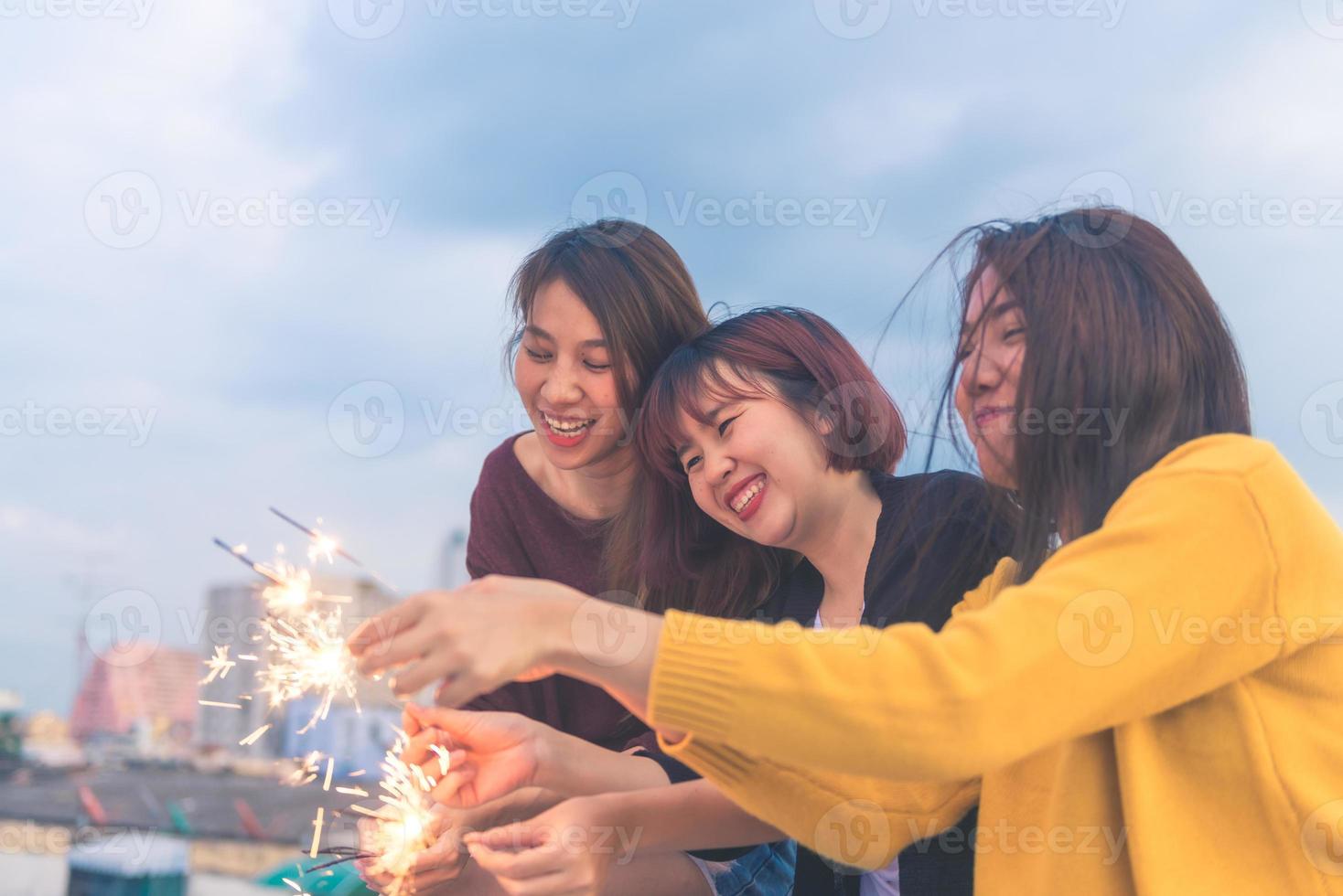 colpo all'aperto di giovani alla festa sul tetto. felice gruppo di amiche asiatiche si divertono e giocano a sparkler alla festa sul tetto al tramonto serale. festa di festa festa di festa. festa di stile di vita adolescenziale. foto