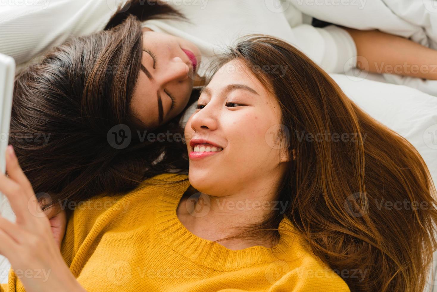 belle giovani donne asiatiche lgbt lesbiche coppie felici che abbracciano e sorridono mentre si trovano insieme a letto sotto la coperta a casa. donne divertenti dopo il risveglio. lgbt coppia lesbica insieme al chiuso concetto. foto