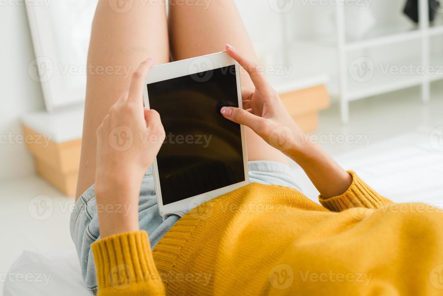 giovane donna asiatica che utilizza tablet simulare schermo nero vuoto nella sua camera da letto da solo facendolo scorrere con il dito nella calda giornata di sole e luce. donna strisciare sul tablet in camera da letto. foto