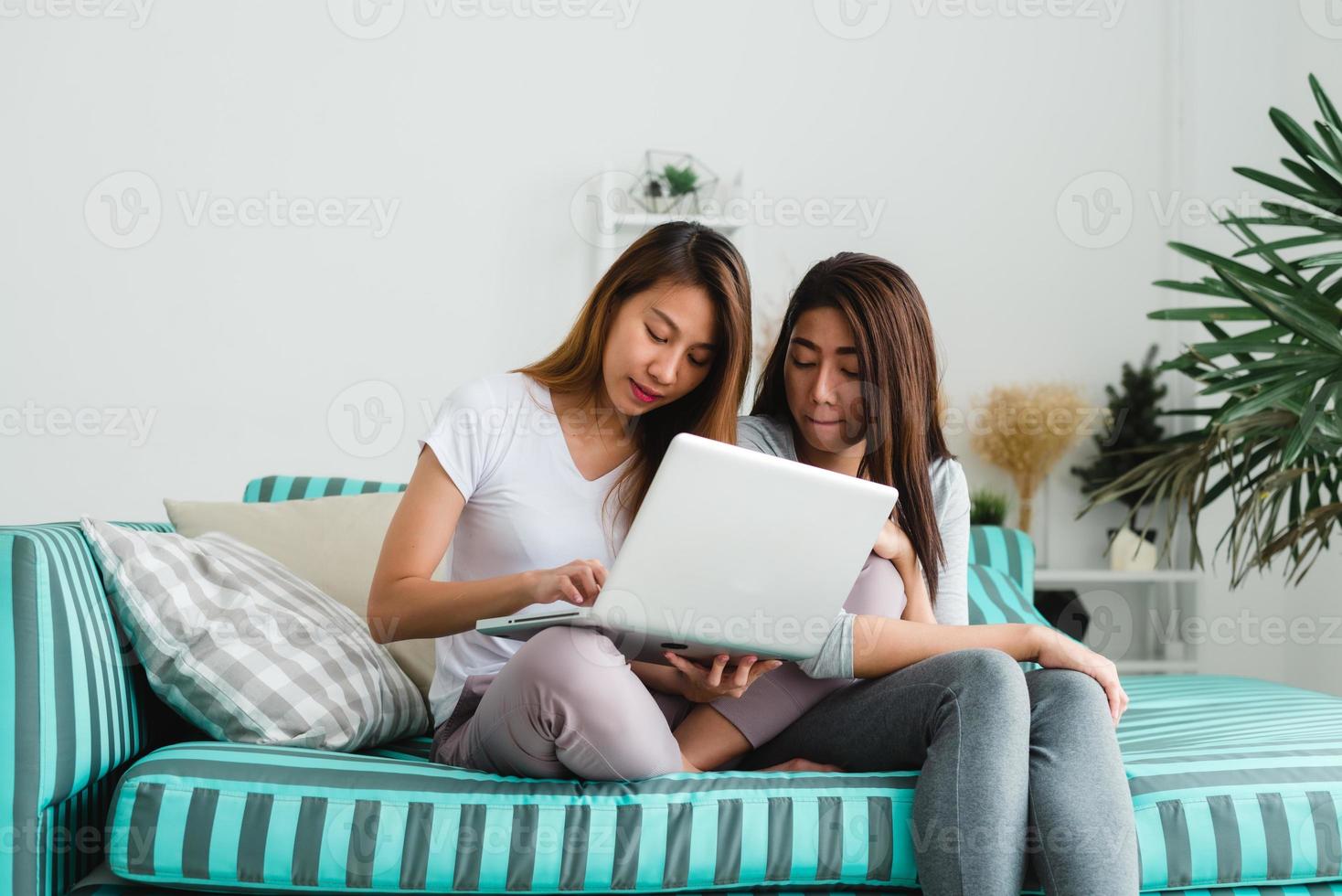 belle giovani donne asiatiche lgbt lesbica coppia felice seduta sul divano acquisto online utilizzando il computer portatile nel soggiorno di casa. lgbt coppia lesbica insieme al chiuso concetto. passare del tempo piacevole a casa. foto