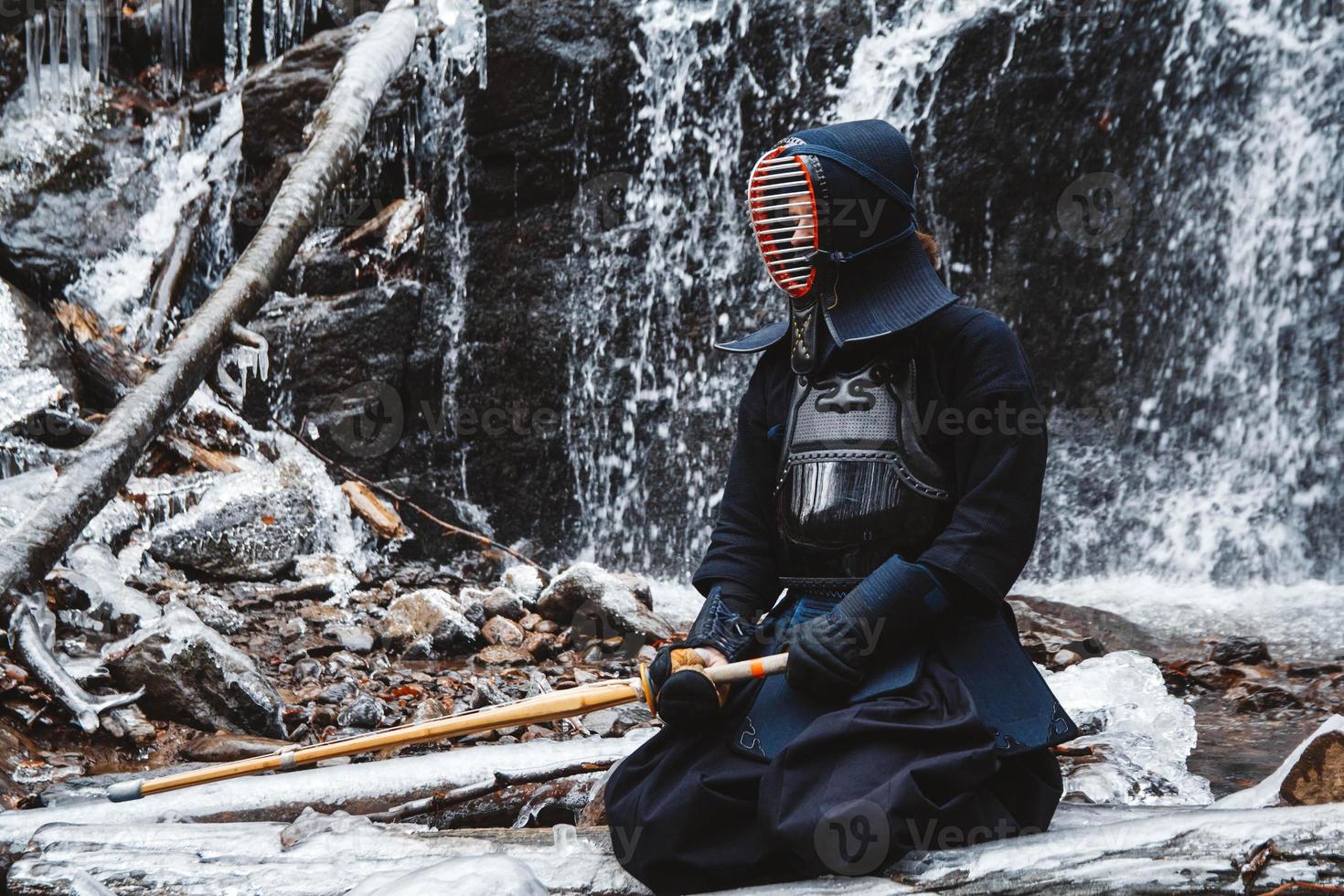 uomo che pratica kendo con spada di bambù su sfondo cascata foto