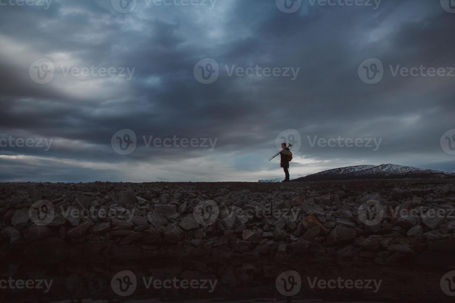 sagoma di viaggiatore maschio con fotocamera su treppiede su sfondo cielo drammatico foto