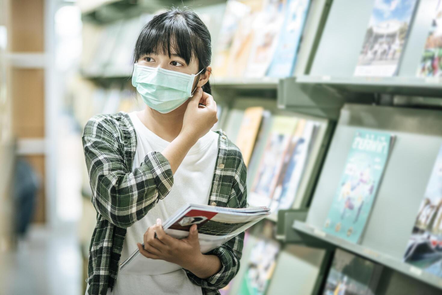 una donna che indossa una maschera e cerca libri in biblioteca. foto