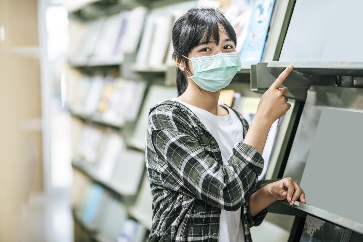 una donna che indossa una maschera e cerca libri in biblioteca. foto