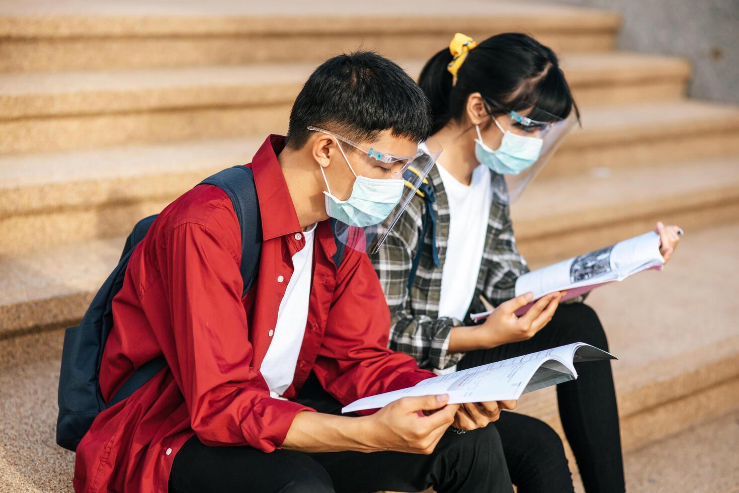 studenti maschi e femmine che indossano maschere si siedono e leggono libri sulle scale foto