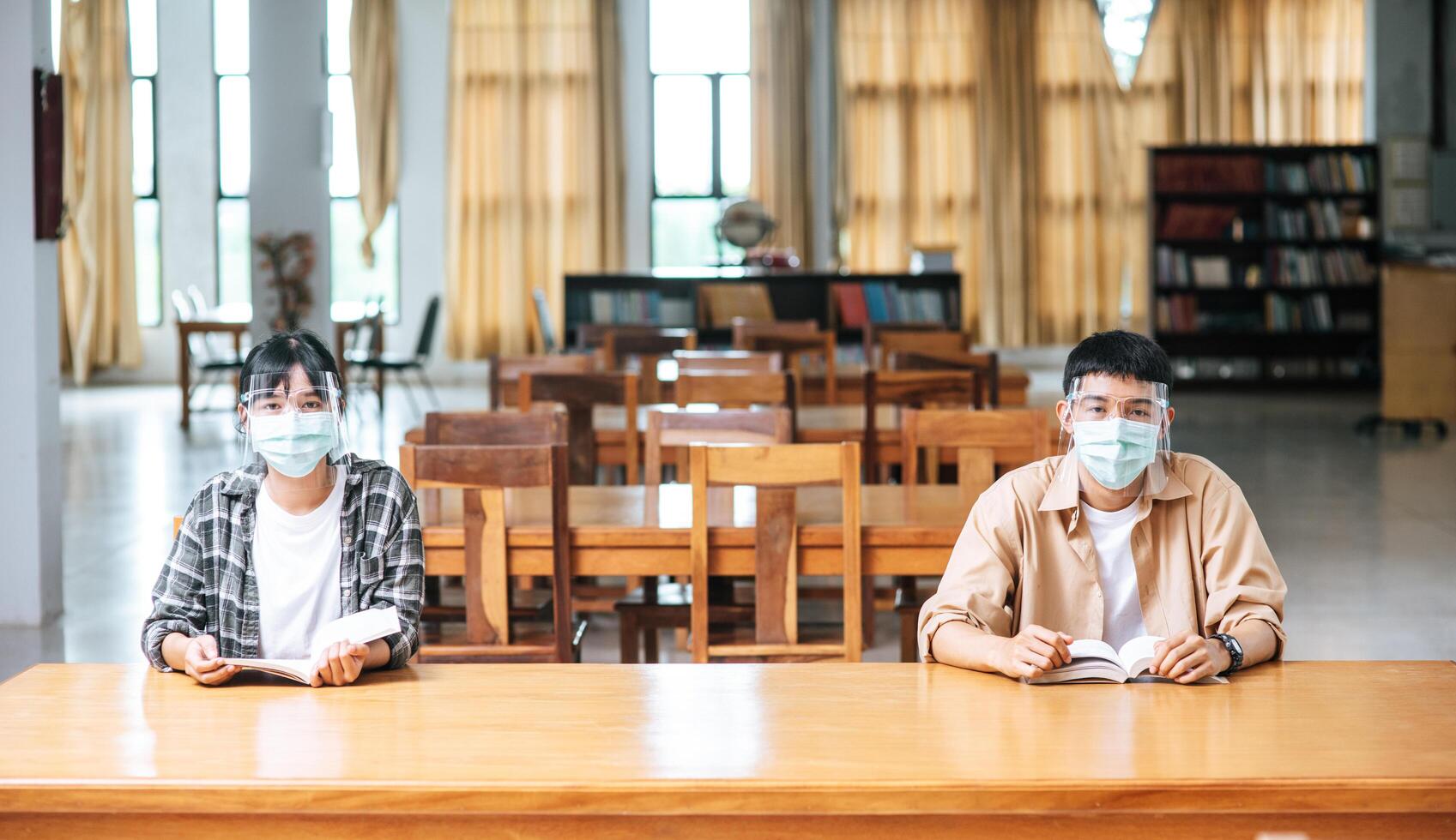 uomini e donne che indossano maschere si siedono e leggono in biblioteca. foto