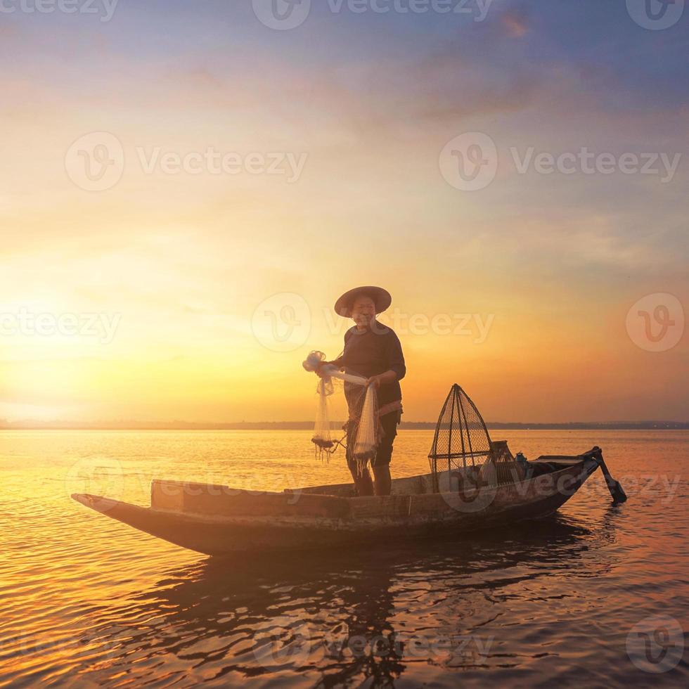 silhouette pescatore asiatico che tiene una rete per catturare pesci d'acqua dolce nel lago naturale durante l'alba foto