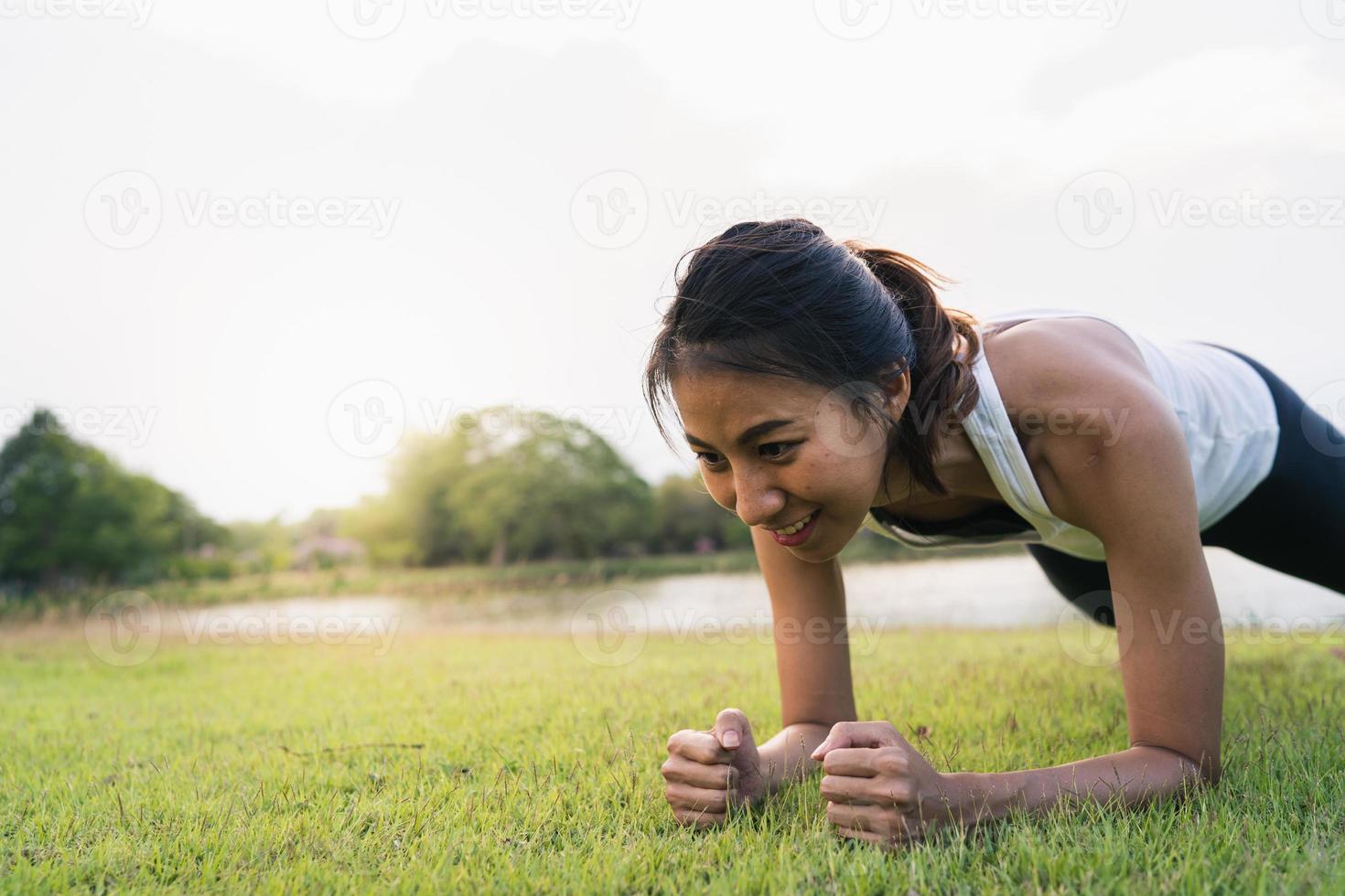 sana giovane donna corridore asiatico riscalda il suo corpo spingendo verso l'alto prima dell'esercizio e lo yoga vicino al lago al parco sotto la calda luce del mattino. fitness lifestyle e donne attive si esercitano nel concetto di città urbana. foto