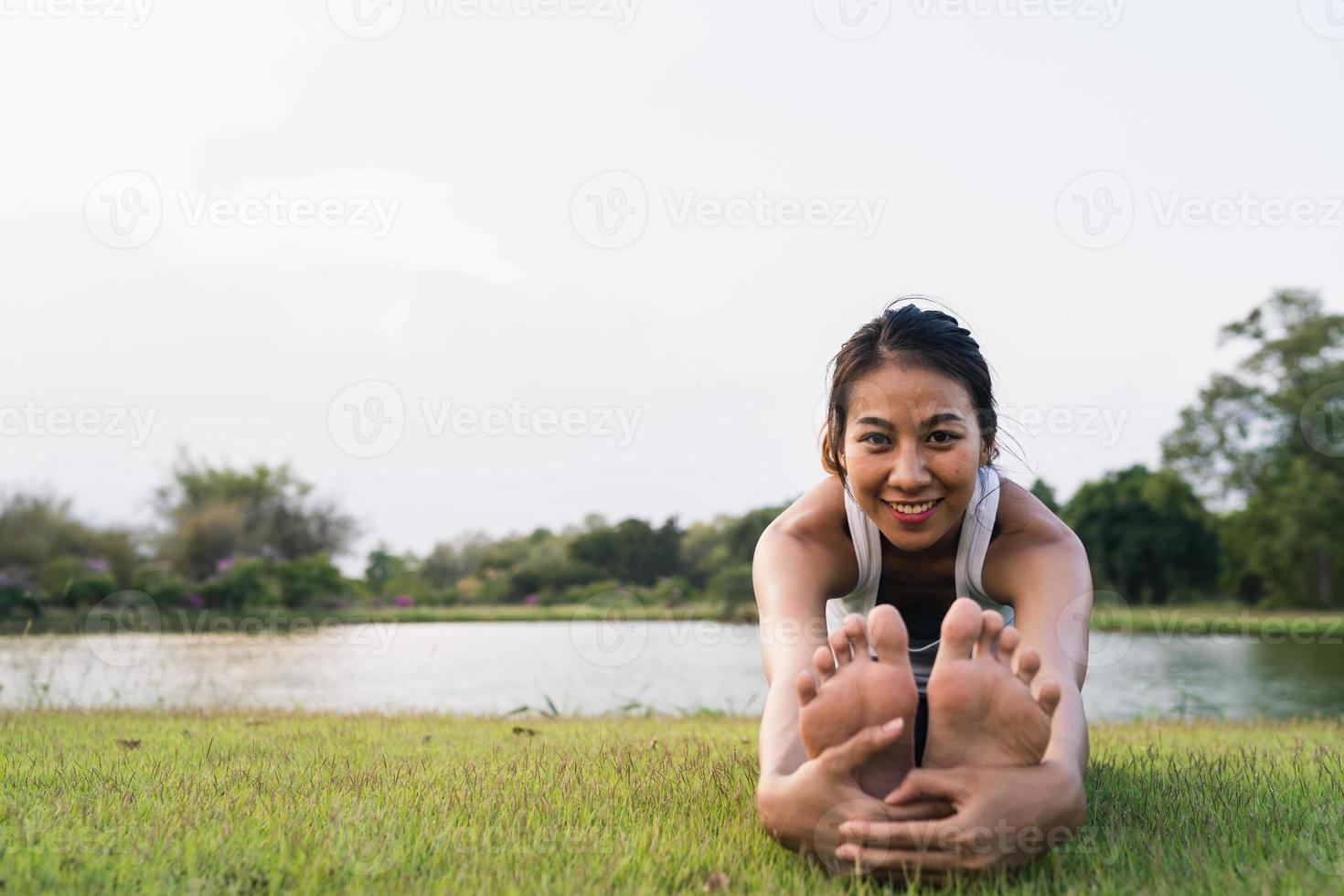 sana giovane donna corridore asiatico riscaldare il corpo che si estende prima dell'esercizio e lo yoga vicino al lago al parco sotto la calda luce del mattino. fitness lifestyle e donne attive si esercitano nel concetto di città urbana. foto