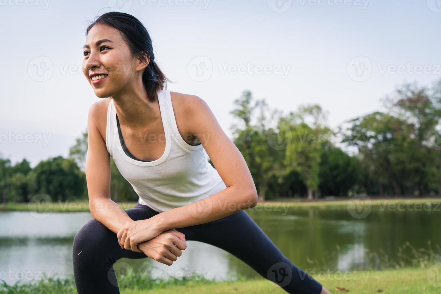 sana giovane donna corridore asiatico riscaldare il corpo che si estende prima dell'esercizio e lo yoga vicino al lago al parco sotto la calda luce del mattino. fitness lifestyle e donne attive si esercitano nel concetto di città urbana. foto