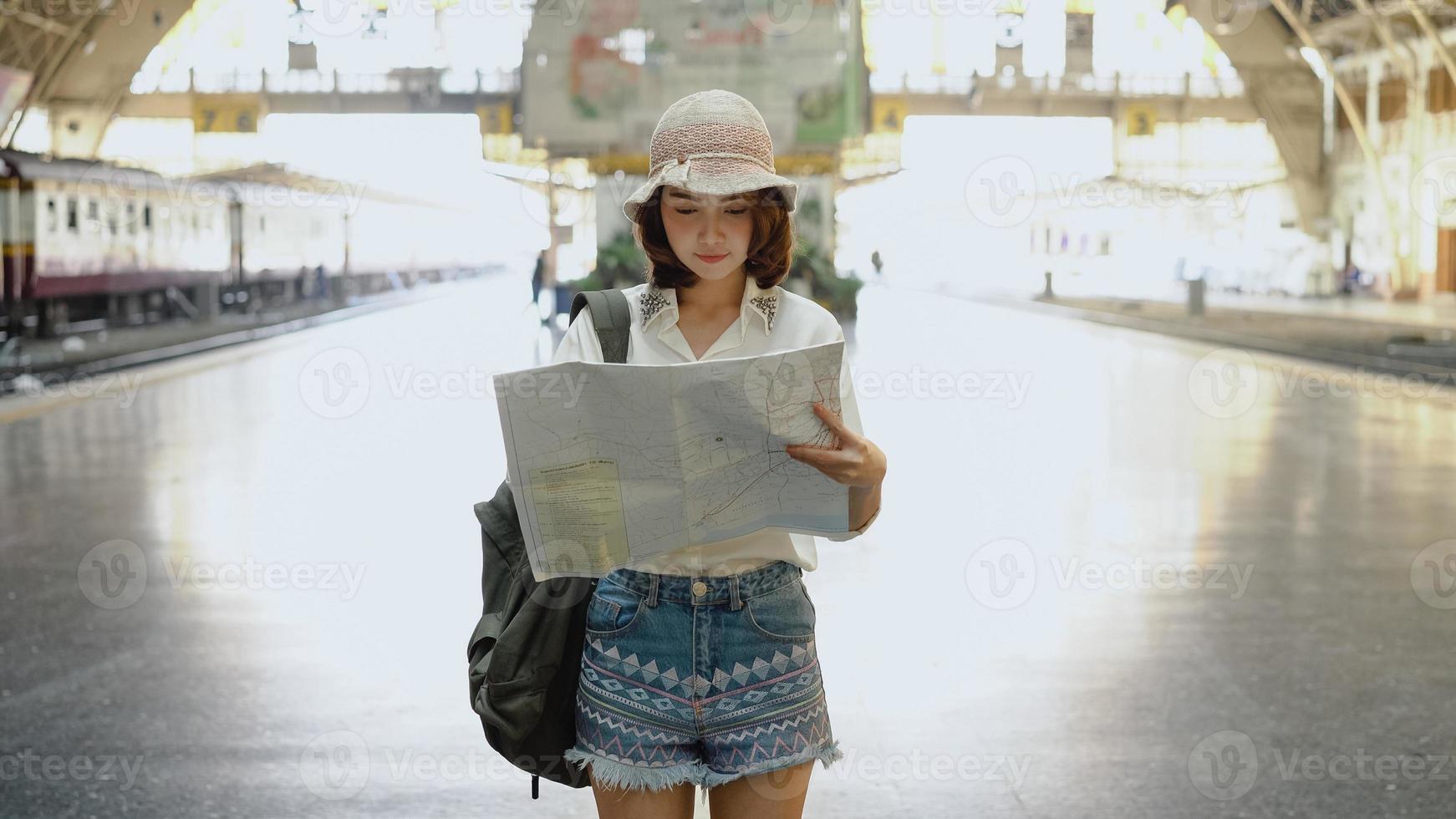 viaggiatore zaino in spalla donna asiatica viaggio a bangkok, thailandia. felice giovane femmina direzione e guardando sulla mappa della posizione alla stazione ferroviaria prima del viaggio. foto