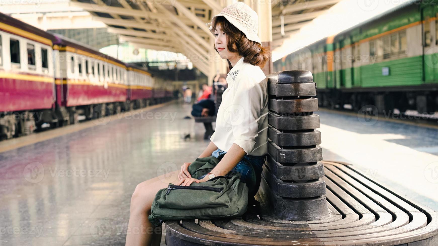 donna asiatica felice che aspetta il treno alla stazione ferroviaria per viaggiare in estate. concetto di viaggio in Thailandia. foto