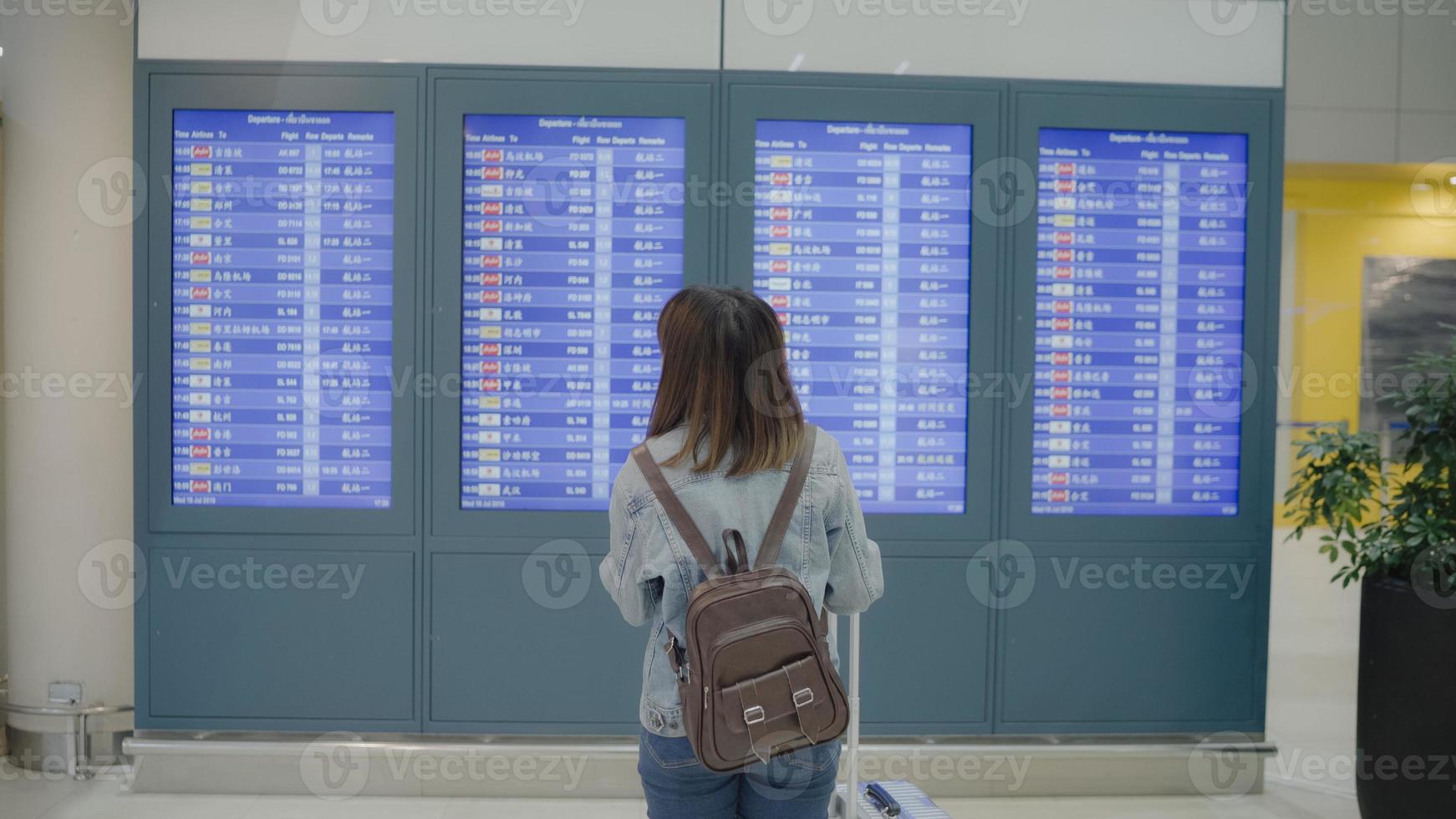 donna asiatica felice che guarda la scheda informativa che controlla il suo volo con i bagagli nella hall del terminal al cancello di partenza dell'aeroporto internazionale. donne di stile di vita felici nel concetto di aeroporto. foto