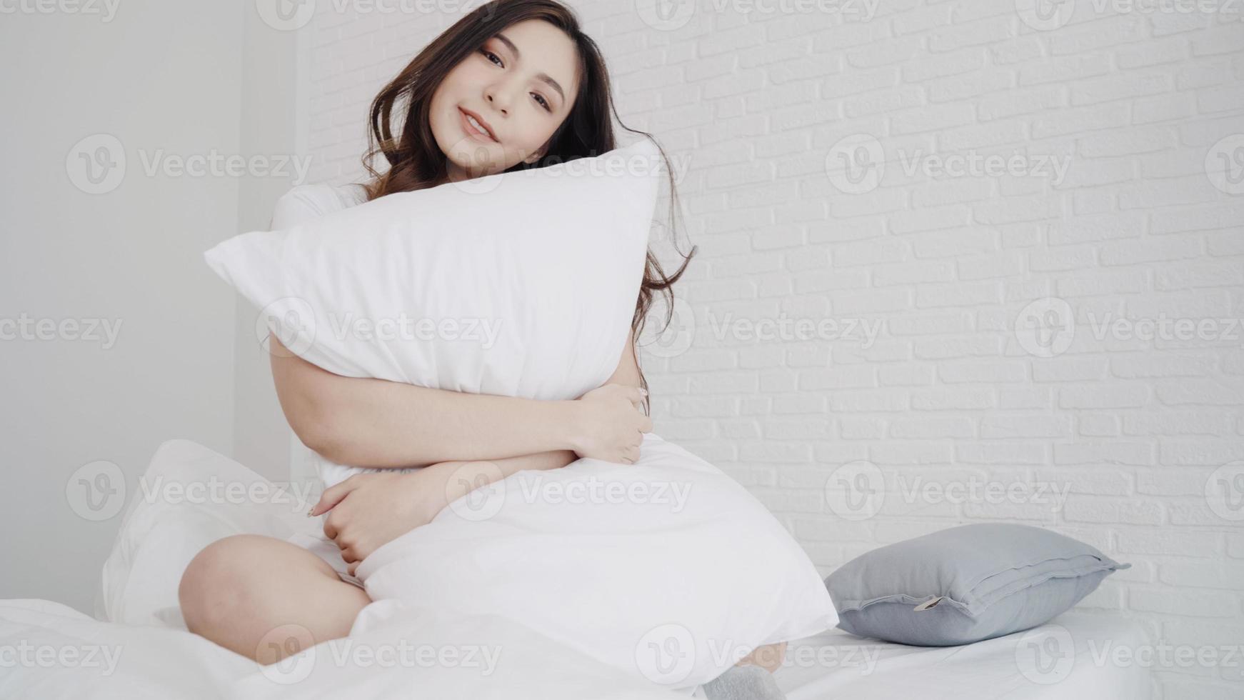 bella donna asiatica che allunga il suo corpo dopo essersi svegliata nella sua camera da letto a casa. la femmina felice gode della mattina soleggiata. stile di vita donna a casa concetto. foto