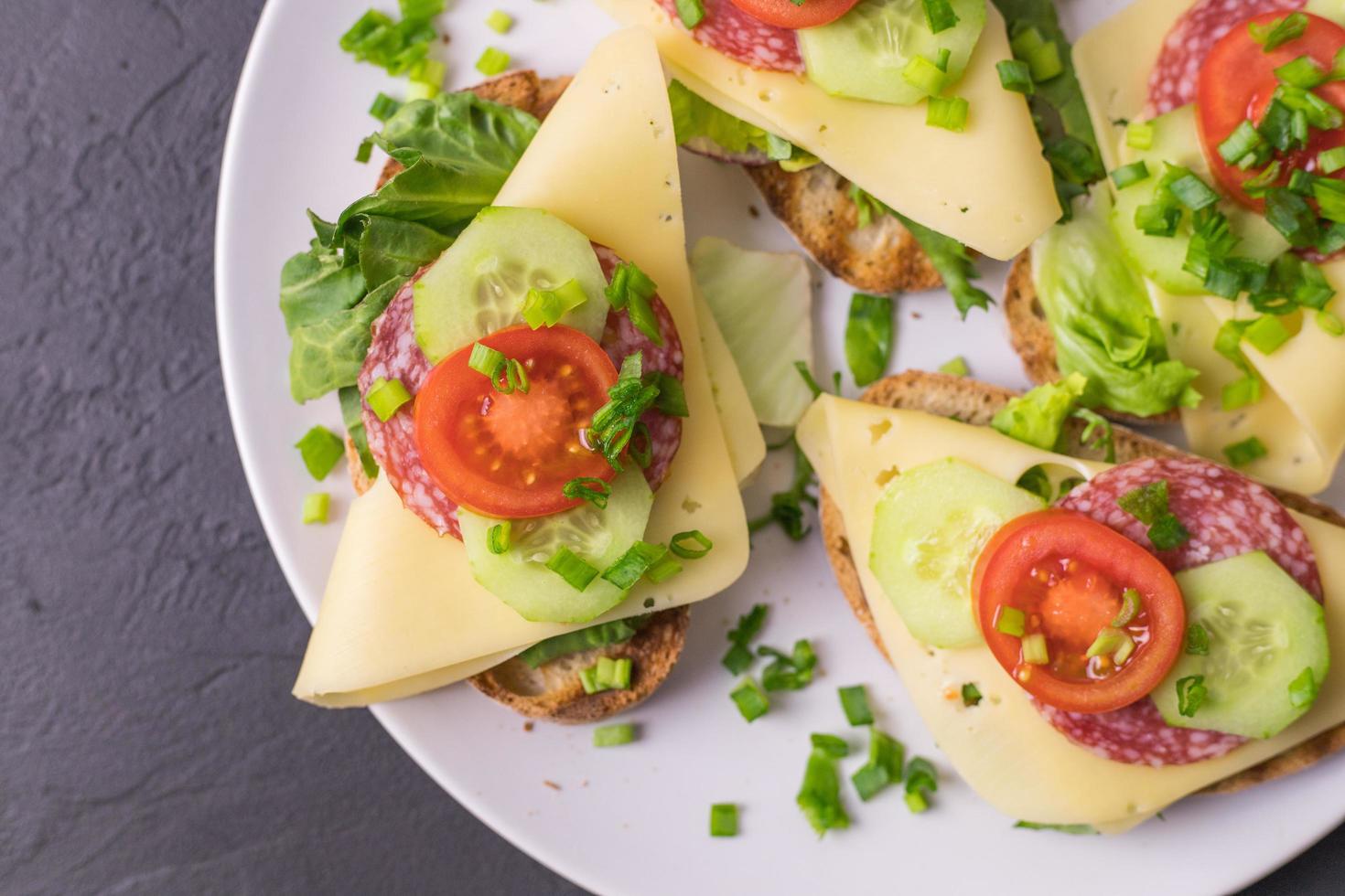 panini salutari primaverili con formaggio, lattuga e pomodoro cosparsi di erba cipollina su piatti adagiati su uno sfondo scuro foto